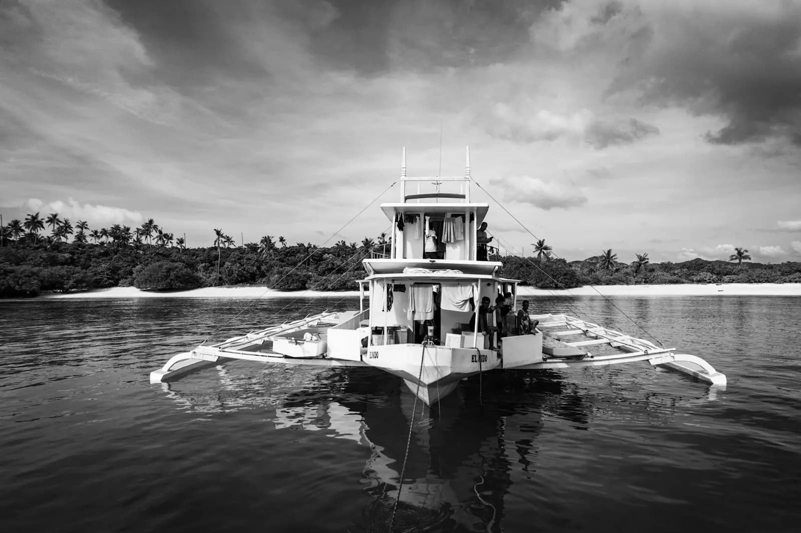 A bangka moored on calm water off a palm-lined island