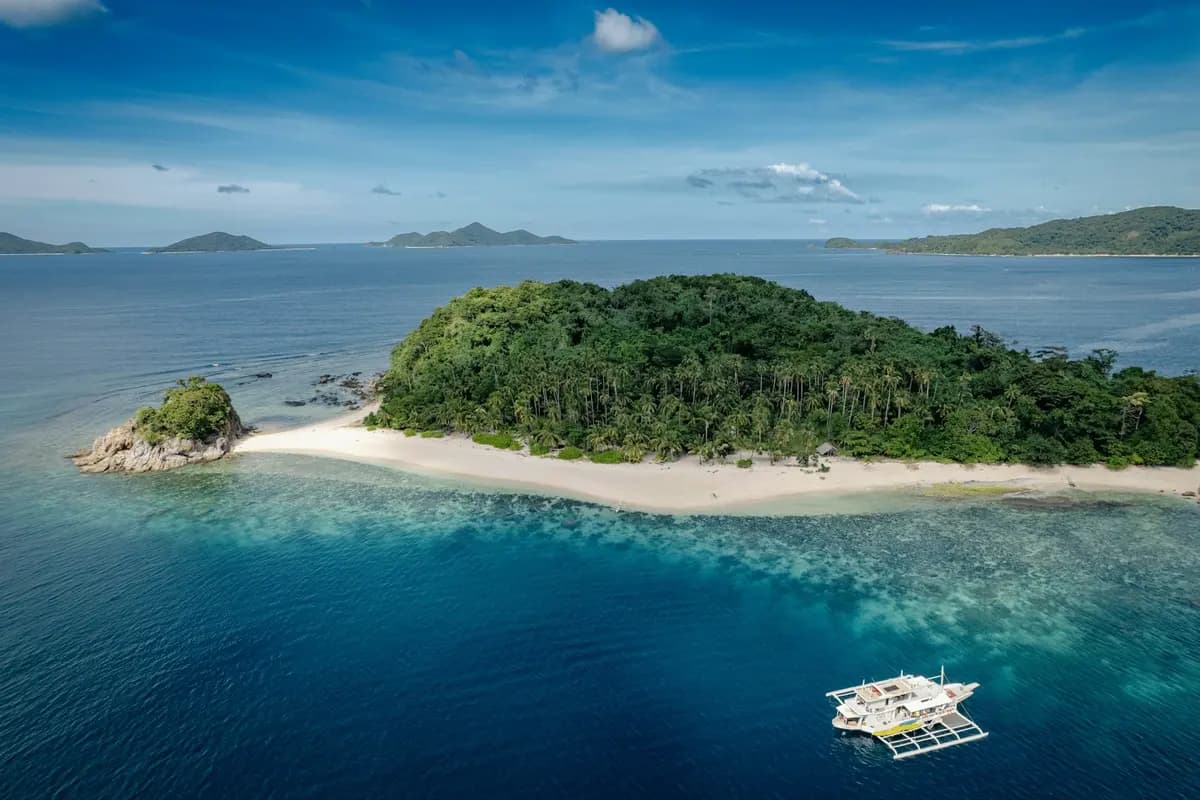 Aerial view of a forested island off Linapacan, Palawan, with a white sandbar and a bangka offshore
